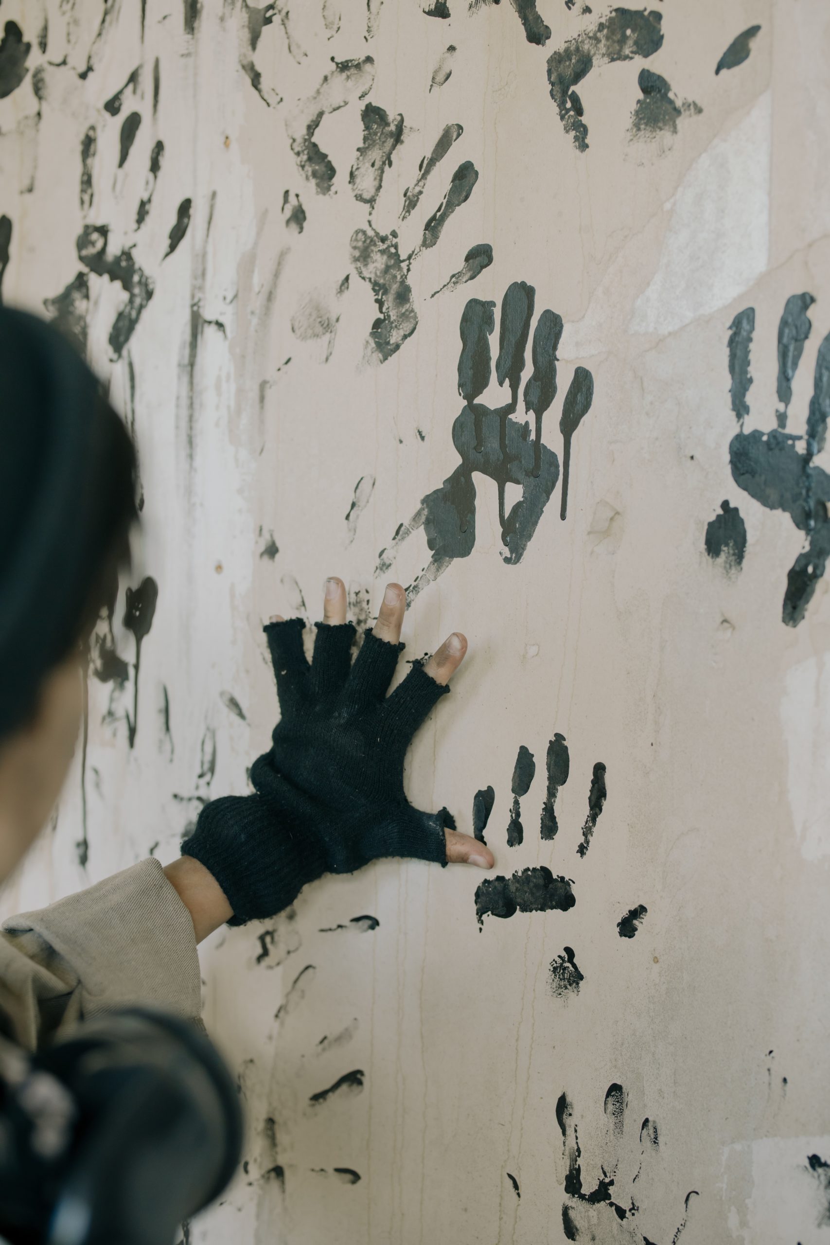 Woman in black gloves making handprints on a wall in black paint