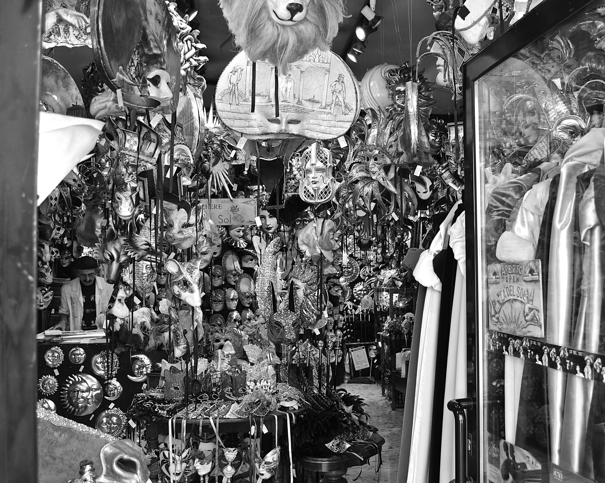 Black and white photo of a shop filled with a variety of Venetian costume masks