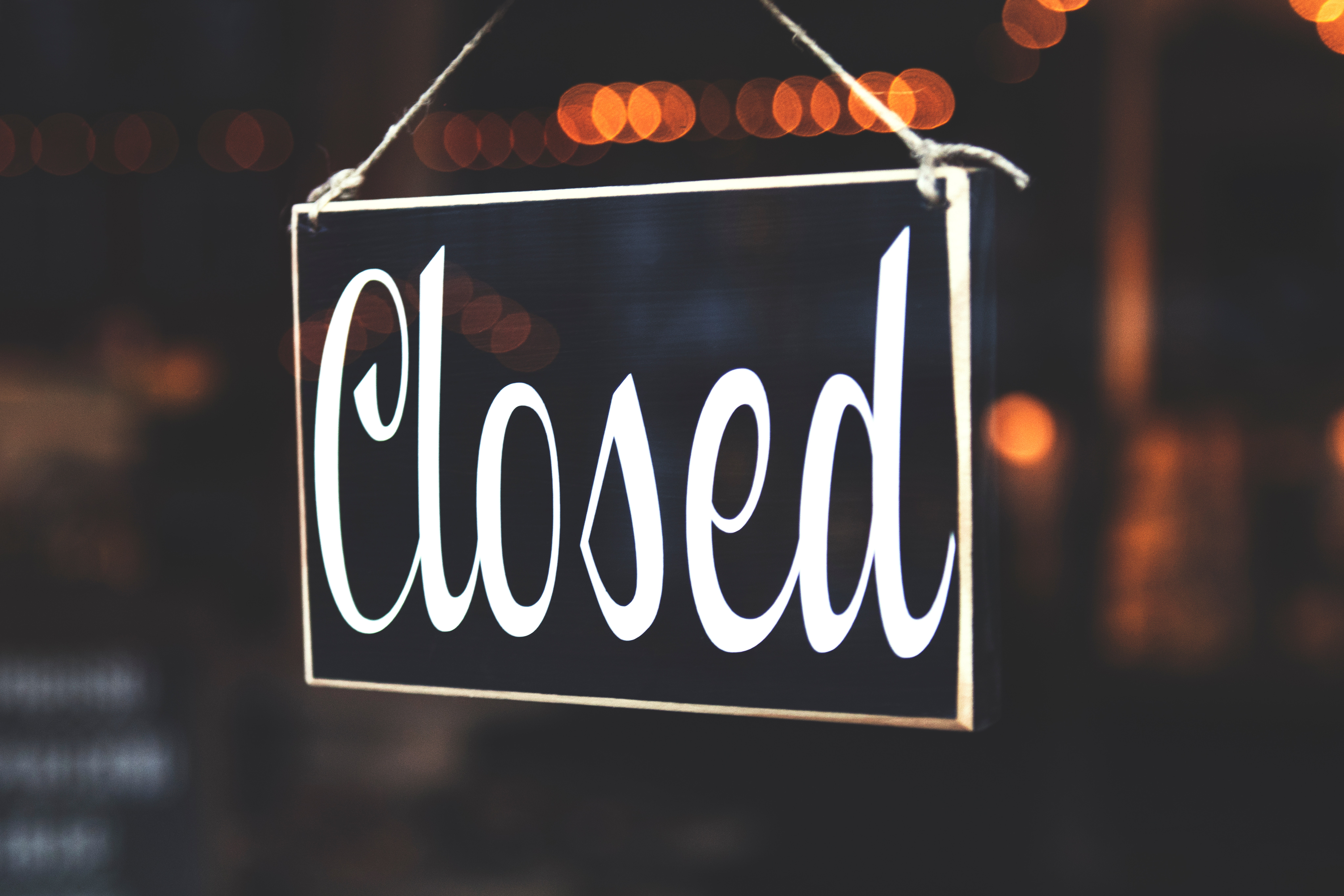 Photo of a sign that reads "closed" in a classy script font with warm lights in the background.
