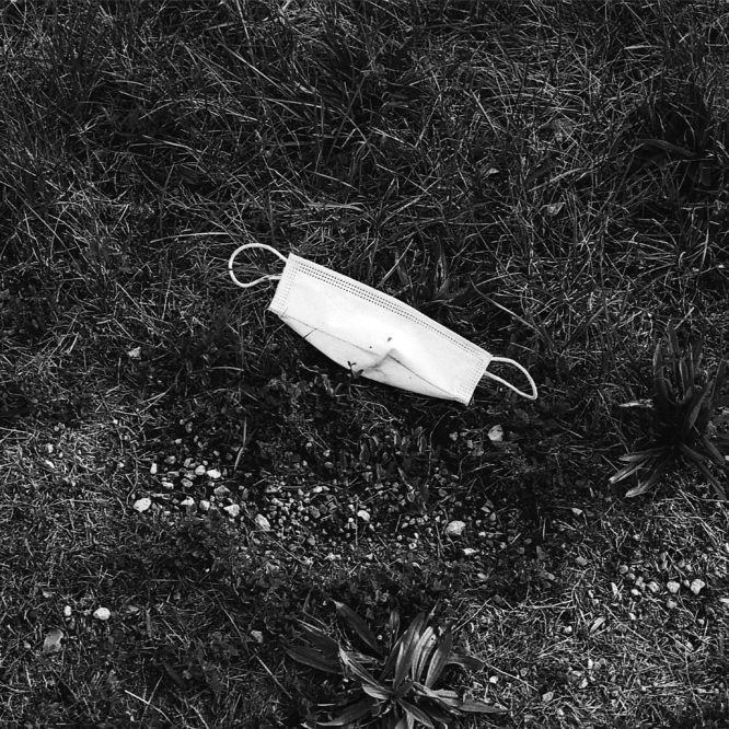 Black and white photo of a surgical mask discarded in the grass