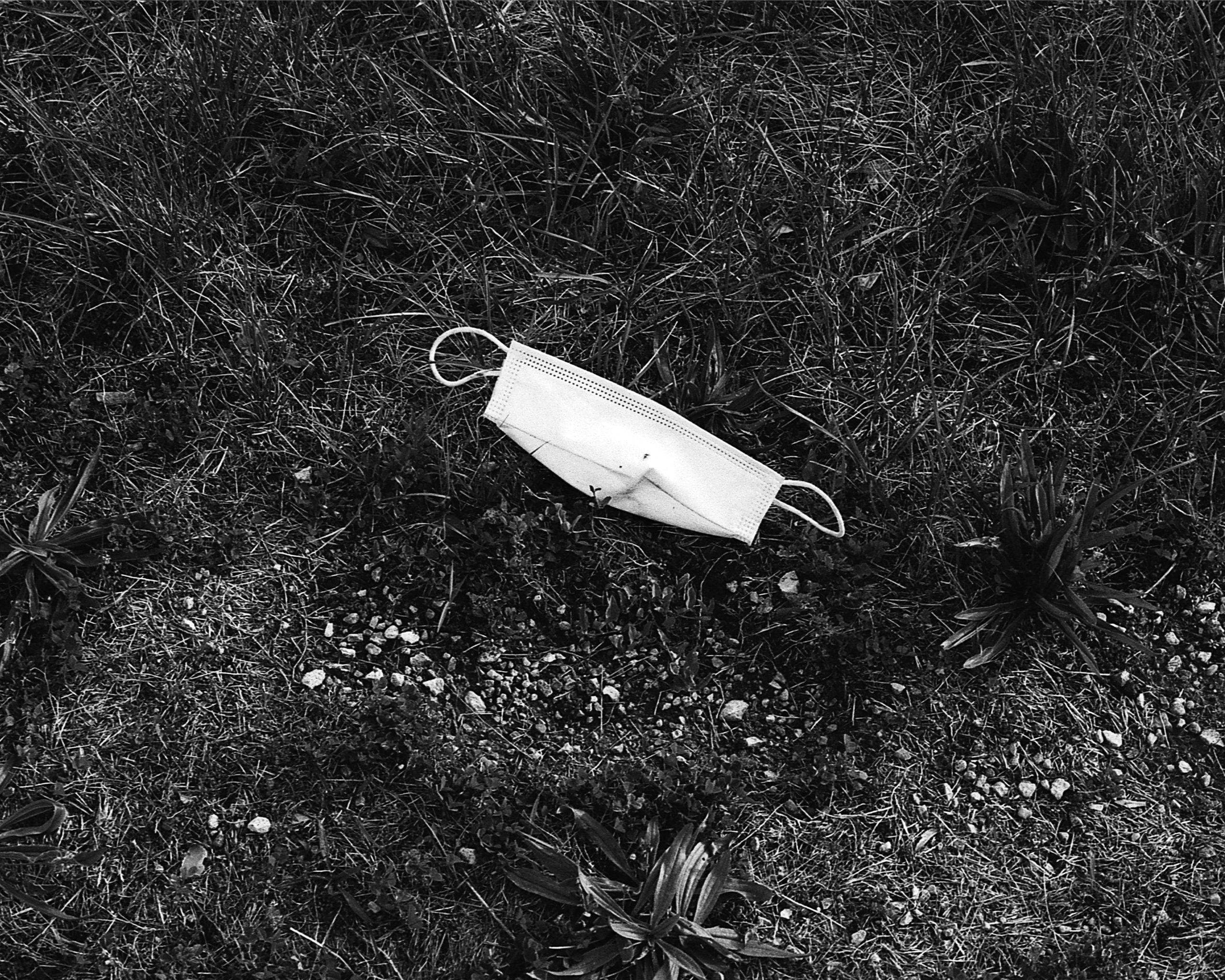 Black and white photo of a surgical mask discarded in the grass