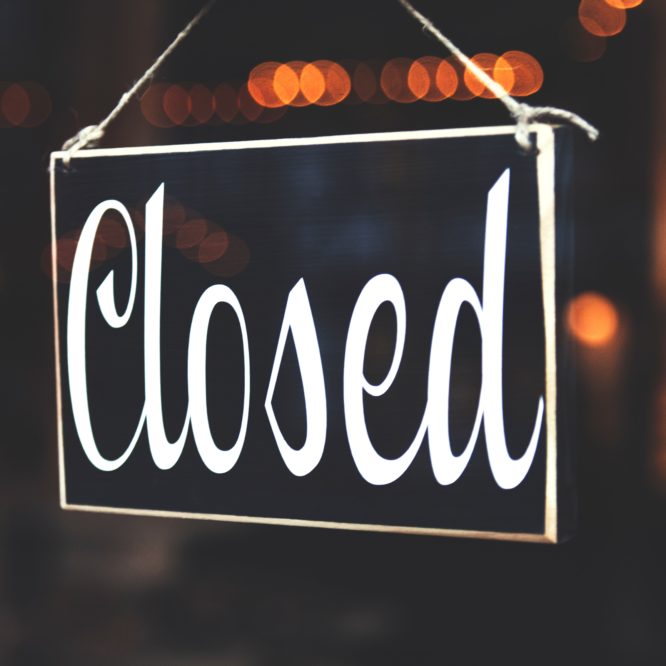 Photo of a sign that reads "closed" in a classy script font with warm lights in the background.